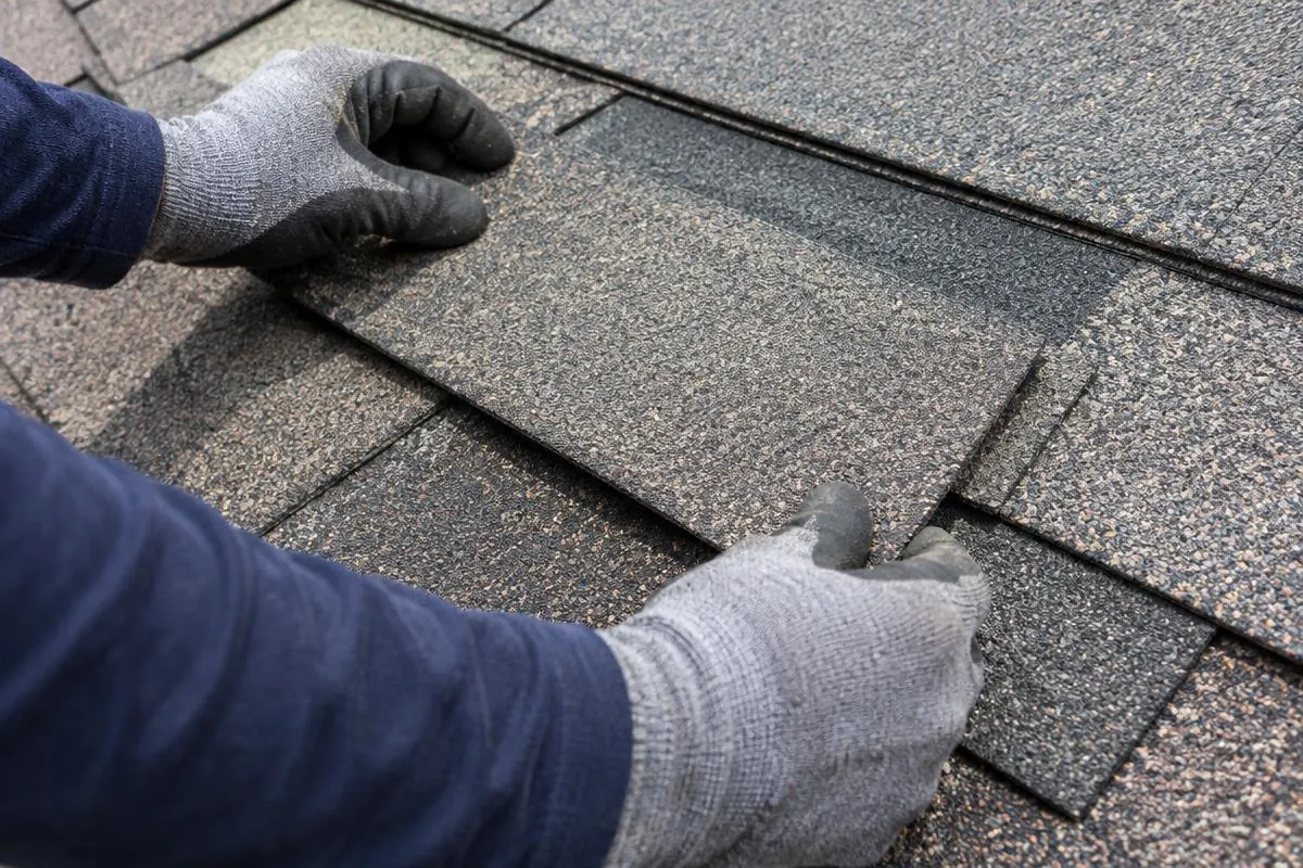 Gloved hands comparing a shingle at a defined repair area