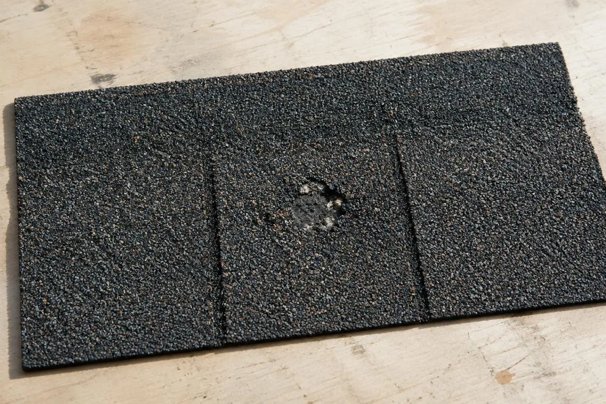 Close view of an asphalt shingle sample with a localized impact mark